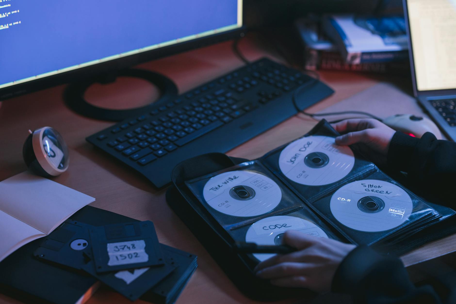 CD being inserted into a sleeve near computer displays with coding interface.